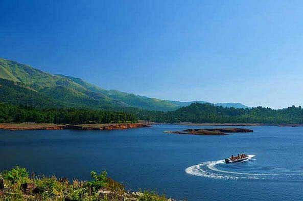 Banasura Sagar reservoir in Wayanad with a motorboat crossing clear waters beneath mist-clad green hills